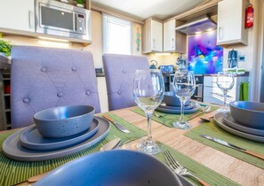 Un coin repas avec une table dressée pour quatre personnes, comprenant des assiettes, des bols et des verres à vin.