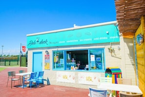 A food stall named 'Deli deck' with a signboard listing items like pizzas, sandwiches, ice creams, cold drinks, and snacks.