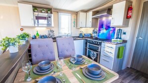 Une cuisine compacte équipée d’un four à micro-ondes, d’une cuisinière et d’un four. Une table à manger est dressée avec deux chaises, des assiettes, des bols et des verres à vin.