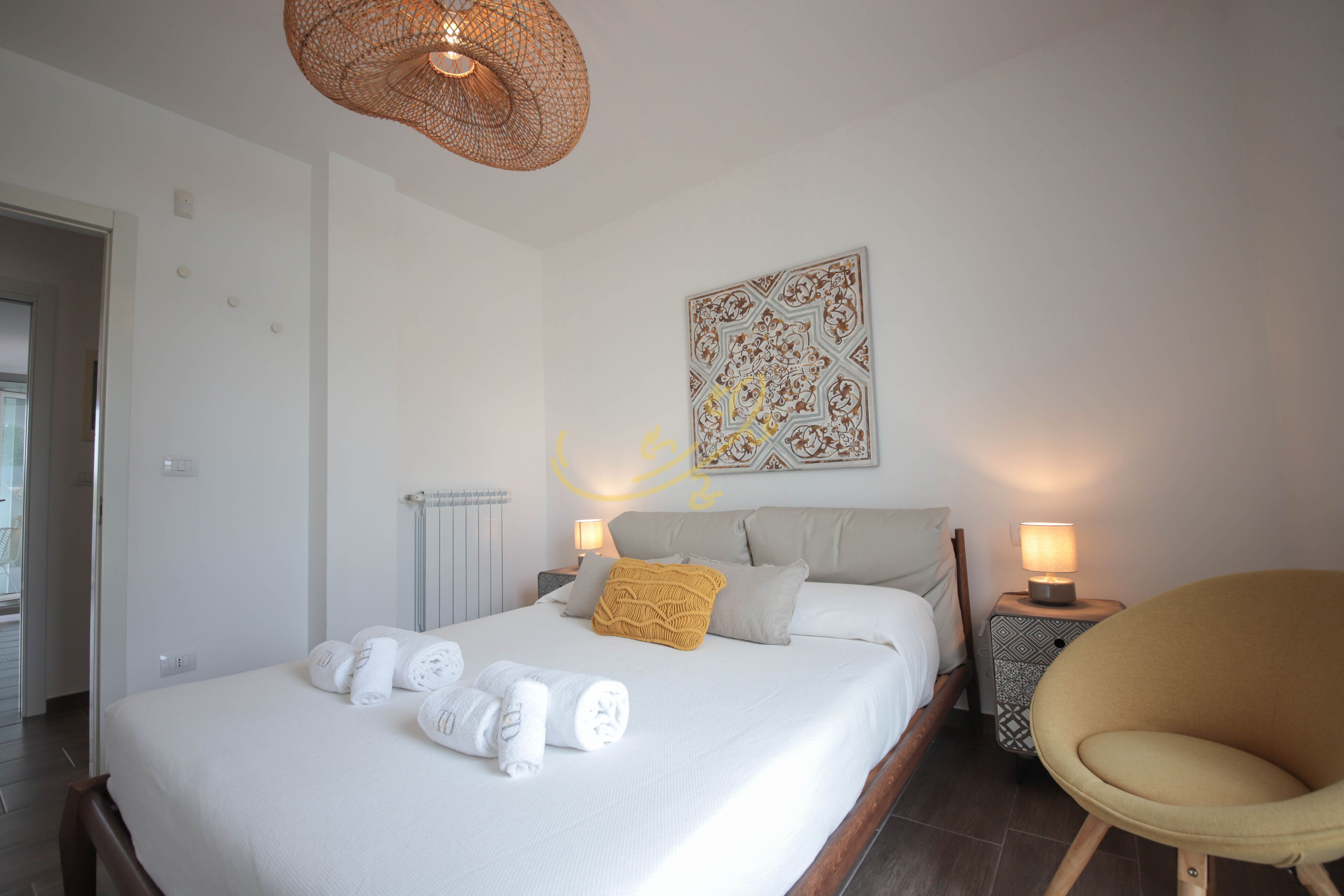 A neatly made bed with towels, a patterned wall hanging, a lamp, and a chair in a hotel room.