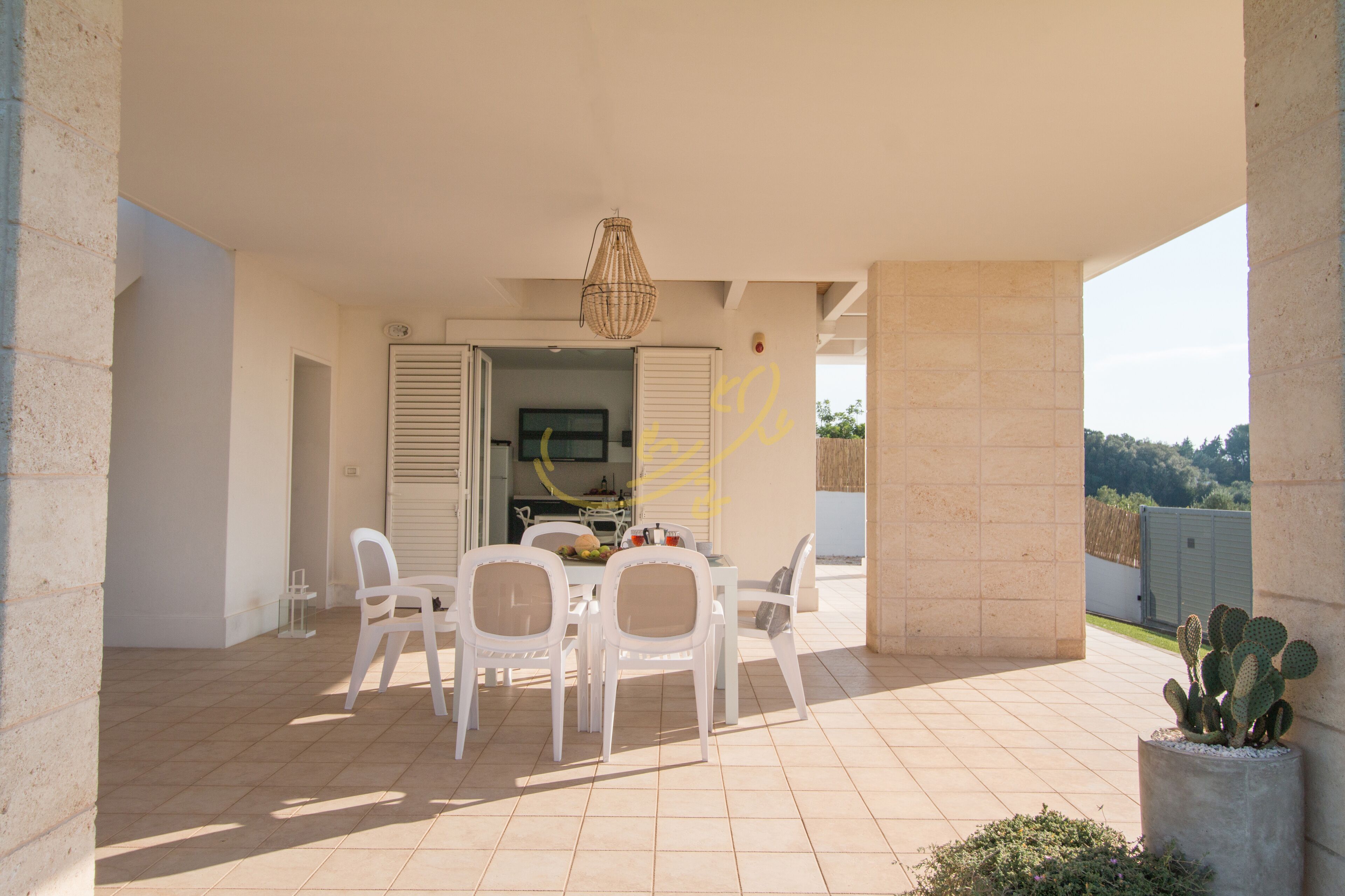 A patio with a table and chairs, a hanging light fixture, and a cactus plant.
