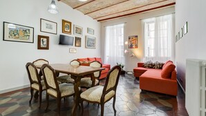 A dining area with a wooden table and chairs, a red sofa, and artwork on the walls. - Monti Colosseum Apartment (Roma)