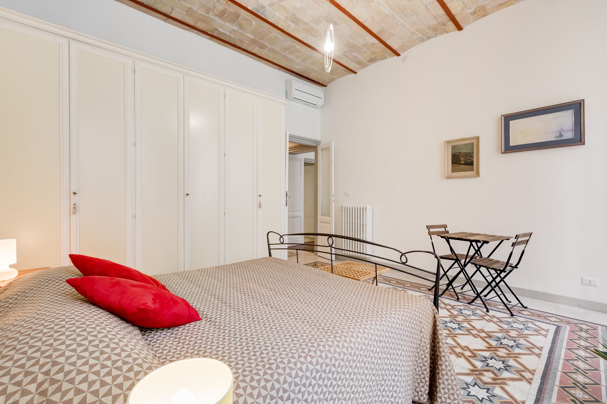 Une chambre à coucher avec un lit, un bureau et des chaises. Il y a deux portes et un appareil de climatisation fixé au mur.