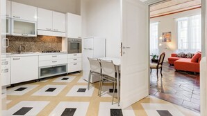 A modern kitchen with white cabinets, a granite backsplash, and a dining area with a table and chairs. - Monti Colosseum Apartment (Roma)