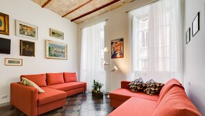A living room with two red sofas, a coffee table, and a potted plant. There are framed pictures on the walls and a large window with sheer curtains. - Monti Colosseum Apartment (Roma)