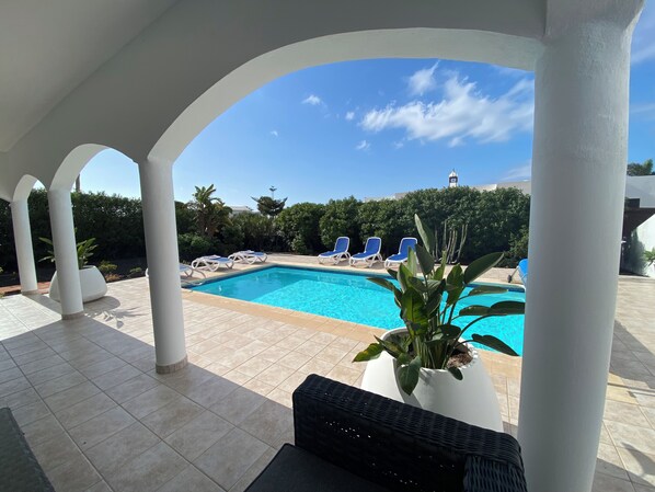 Ein Poolbereich mit blauem Himmel, weißen Säulen und blauen Liegestühlen.
