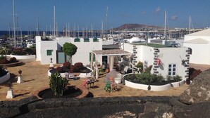 Ein Küstengebäude mit einer Terrasse, einem kleinen Garten und Blick auf eine Marina mit zahlreichen Booten.