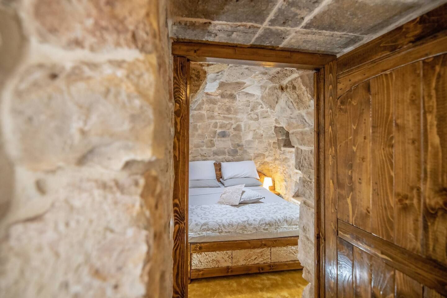 Ein Zimmer mit Steinwänden, einem Bett und einer Holztür.