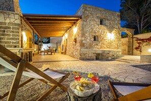 Un espace extérieur aménagé en terrasse, avec des murs en pierre, une pergola en bois et une table où sont disposés des en-cas.