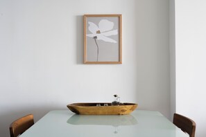 Una mesa de comedor con un cuenco de madera como centro, una obra de arte en la pared y dos sillas.