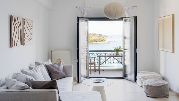 A modern living room with a sofa, a small round table, and a view of the sea through a glass door. - Footsteps to the beach! (Agios Nikolaos)