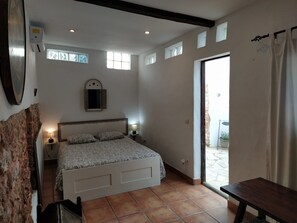 Ein Schlafzimmer mit Bett, Nachttischlampen, einer Wand-Klimaanlage, einem Fenster mit Rollläden und einer Tür zu einem Außenbereich.