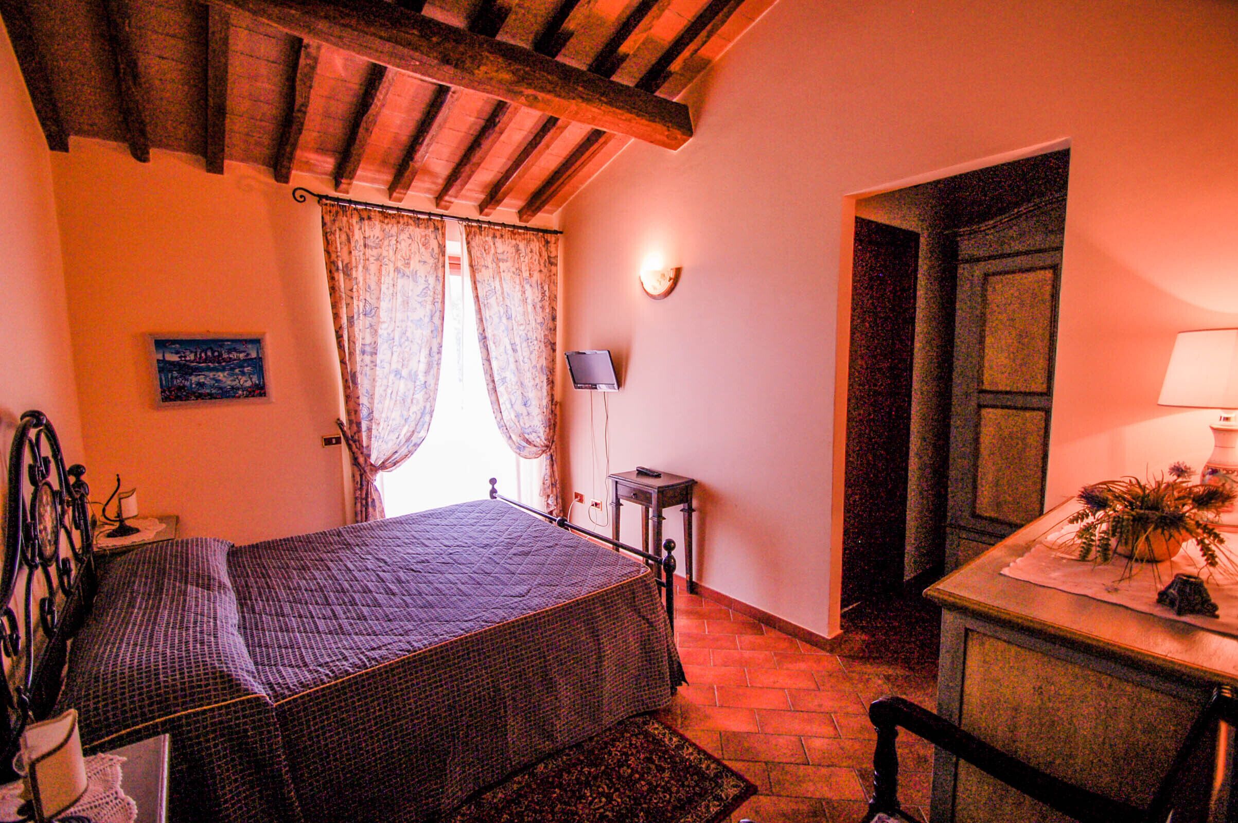 A bedroom with a bed, a bedside table, a lamp, a small table with a plant, and a door.