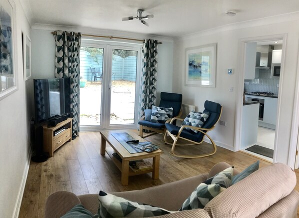 A living room with a TV, sofa, coffee table, and rocking chair. There is a sliding glass door leading to a backyard.