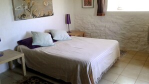 Quarto com cama, mesa de cabeceira, luminária, pintura e janela com cortinas.