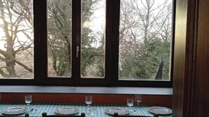 A dining area with a table set for four, a window with a view of trees, and a checkered tablecloth. - House / Villa - BOLSENA (Bagnoregio)