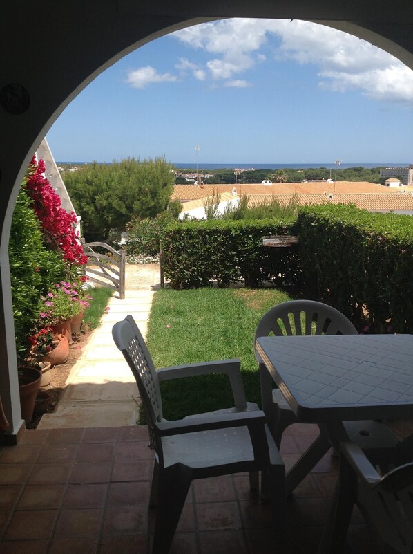 An outdoor patio with a table and chairs, a pathway leading to a view of the sea, and potted plants. - Apartment with Pool and Gardens (Arenal d'en Castell)