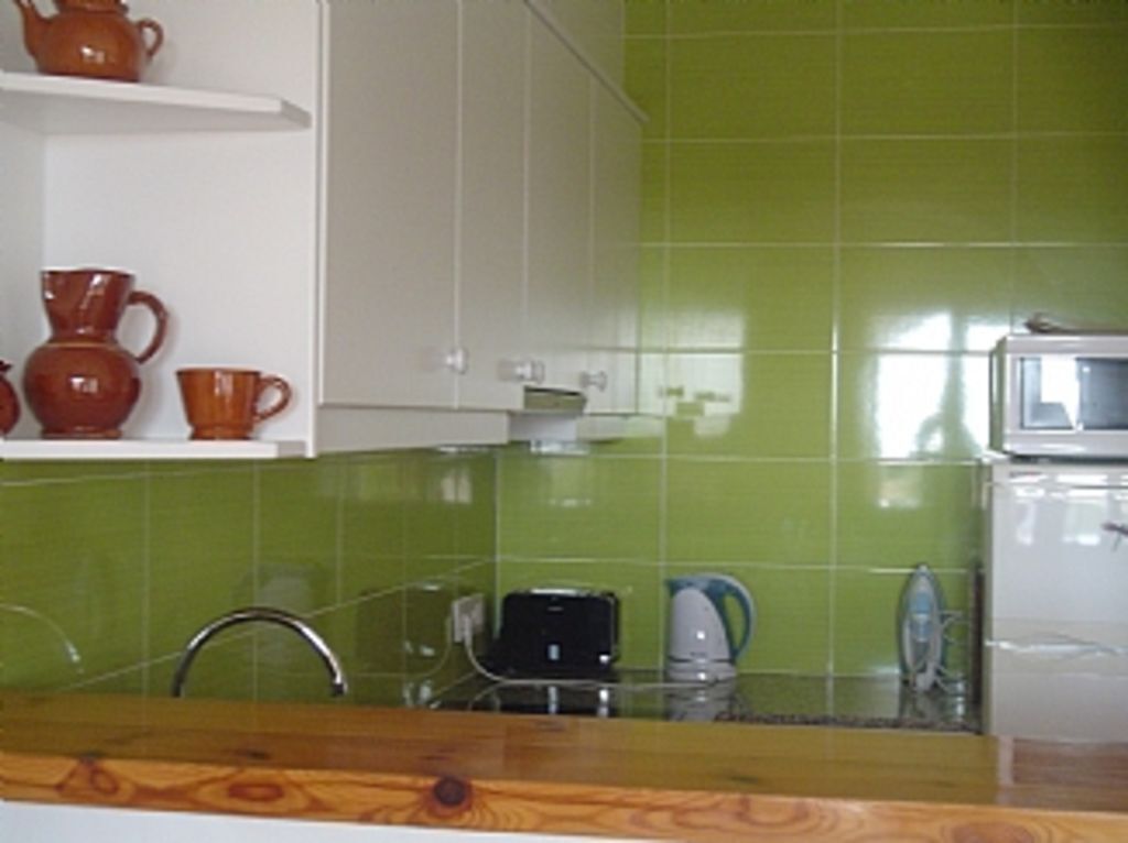 Une cuisine avec des carreaux verts, un four à micro-ondes et une étagère avec des tasses rouges.