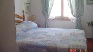 A bedroom with a bed, a window with curtains, a bedside table with a lamp, and framed pictures on the wall.