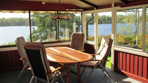 Un porche cubierto con una mesa de madera y cuatro sillas, con vista a un lago.