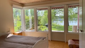 Un dormitorio con cama, una silla y grandes ventanas con vistas a un jardín y un lago.