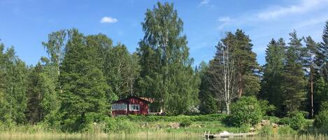 Järven rannalla sijaitseva mökki, jonka ympärillä on tiheä metsä.