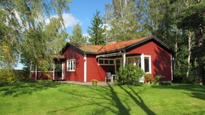 Una casa de madera roja con un porche, rodeada de árboles y césped.
