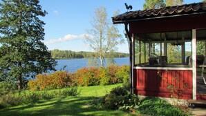 Una cabaña junto al lago con un porche cubierto, vista al lago y follaje circundante.