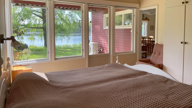 Un dormitorio con un ventanal grande con vistas a un lago, una cama con edredón estampado y techo de madera.