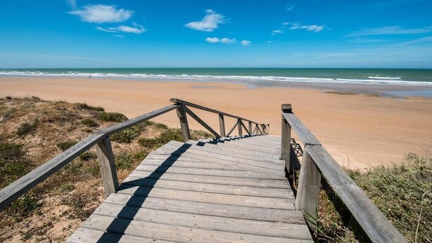 Una escalera de madera que lleva a una playa con cielos despejados.