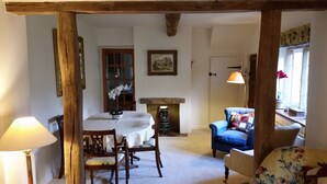 A cozy room with a wooden ceiling, a dining table with chairs, a blue armchair, a lamp, and a fireplace.
