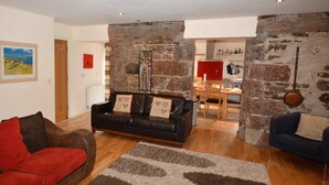 A living room with a brown leather sofa, a red sofa, and a blue sofa. There is a stone wall and a wooden floor. - Spacious Riverside Cottage Perfect For Families, groups,pets. ** NEW HOT TUB** (Glasgow)
