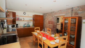 A compact kitchen with wooden cabinets, a dining table set for four, and a built-in cabinet with glassware. - Spacious Riverside Cottage Perfect For Families, groups,pets. ** NEW HOT TUB** (Glasgow)