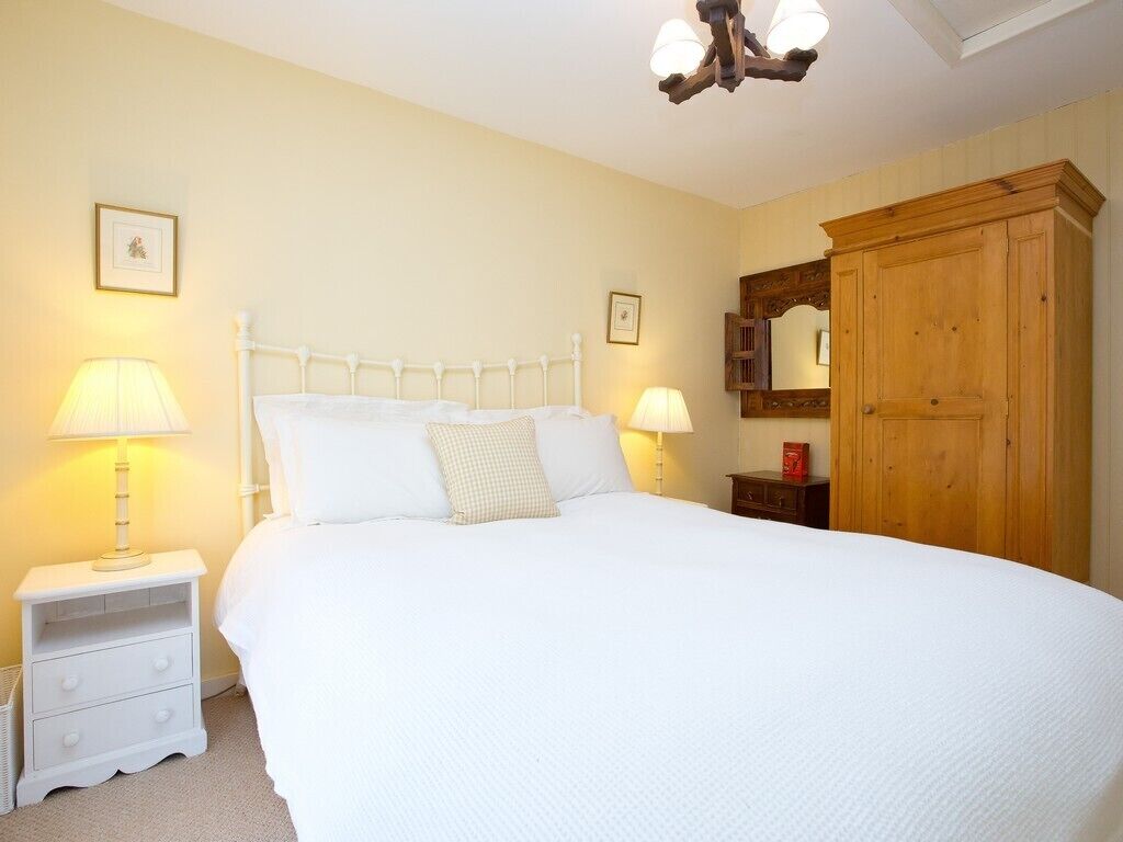 A neatly made bed with white linens, two bedside lamps, a wooden wardrobe, and a framed picture on the wall.