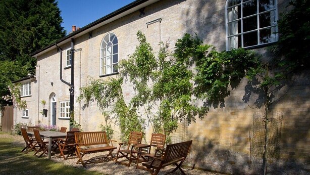 A stone building with a garden patio featuring wooden furniture and climbing plants.