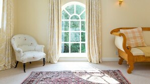 A room with a large arched window, a white armchair, a wooden sofa, and a patterned rug.