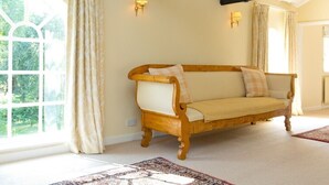 A room with a wooden sofa, a patterned rug, and a large window with curtains.