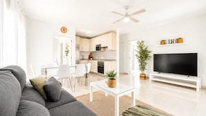 Ein modernes Wohnzimmer mit einer Couch, Fernseher und einem Essbereich mit Stühlen und einem Tisch.