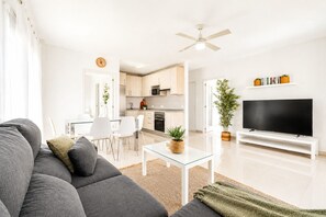 A modern living room with a sofa, TV, and a dining area with chairs and a table.