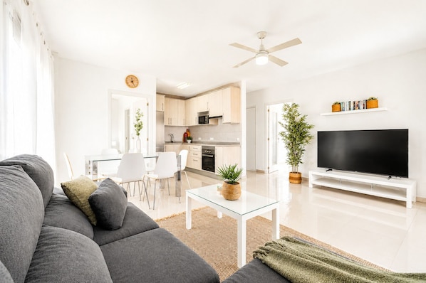 A modern living room with a sofa, TV, and a dining area with chairs and a table.