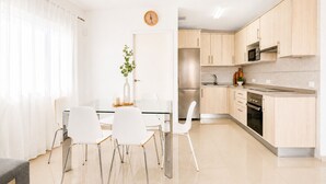 Eine moderne Küche mit hellen Holzschränken, Edelstahlgeräten und einem Essbereich mit weißen Stühlen und einem Glastisch.