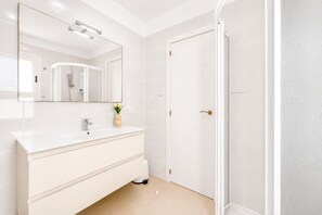 A bathroom with a white vanity, a mirror, a shower, and a door.