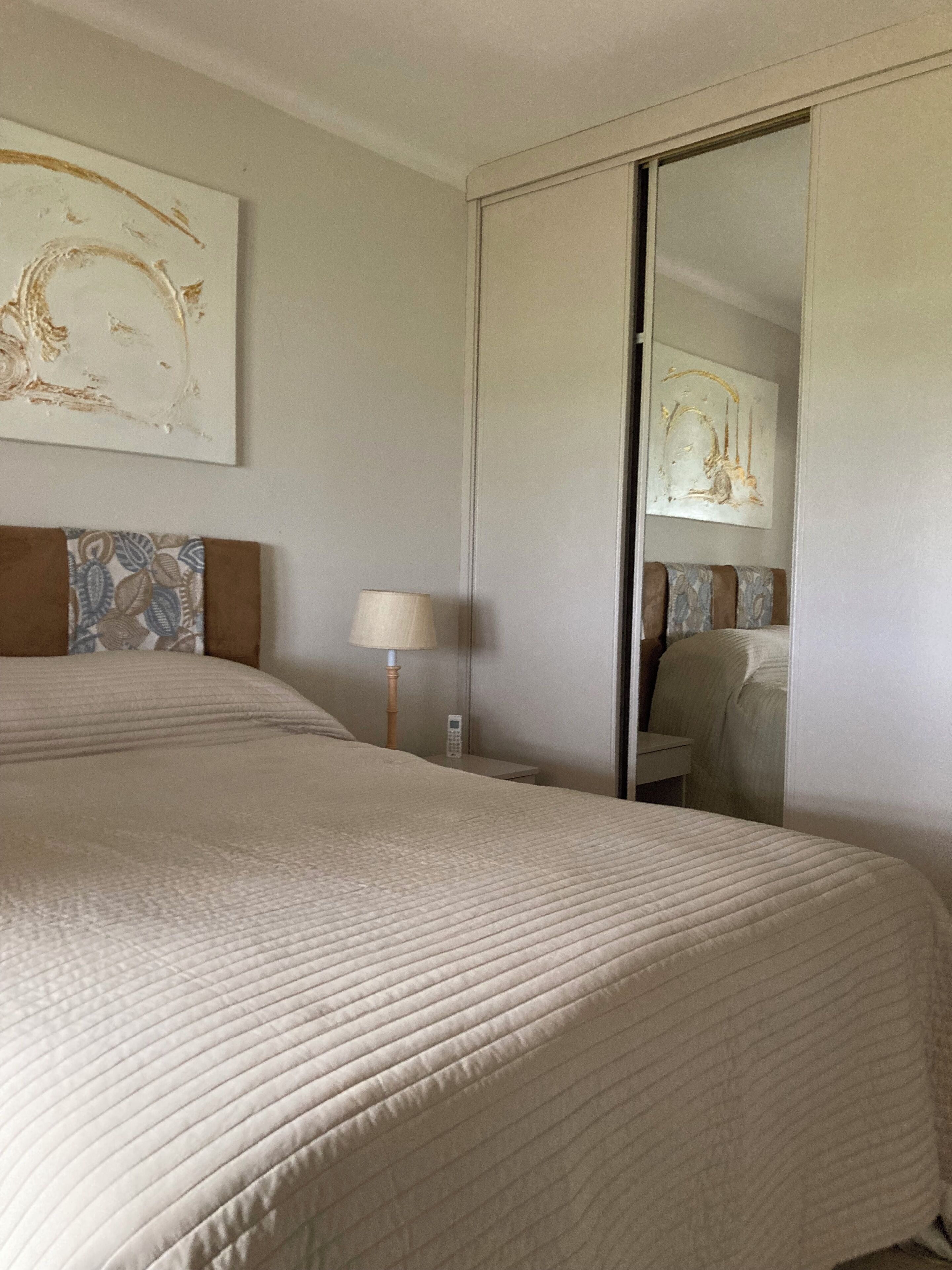 A hotel room with a large bed, a bedside table with a lamp, and a wardrobe.