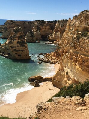 A coastal landscape with rocky cliffs, clear turquoise water, and a sandy beach.