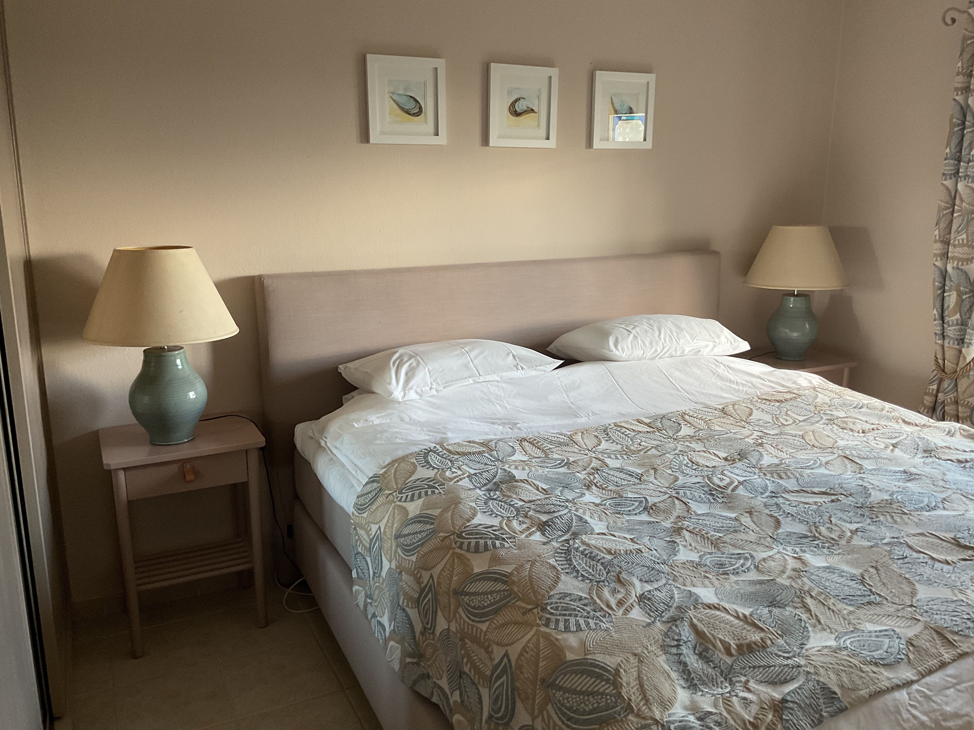 A hotel room with a bed, two bedside lamps, a nightstand, and three framed pictures on the wall.