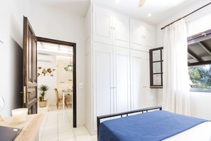 Un dormitorio con cama, armario, escritorio con lámpara y ventana con cortinas.