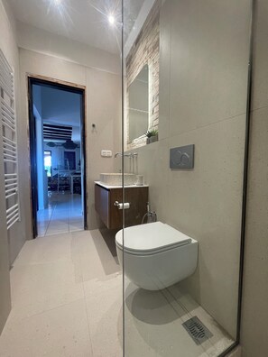 Un baño moderno con ducha de vidrio, inodoro blanco y tocador de madera.