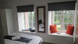 A bedroom with a bed, a window seat with pillows, a mirror, and a view of greenery outside. - LARGE 4 BEDROOM FARMHOUSE  lots of charm, fully renovated 8+ (Bréhan)