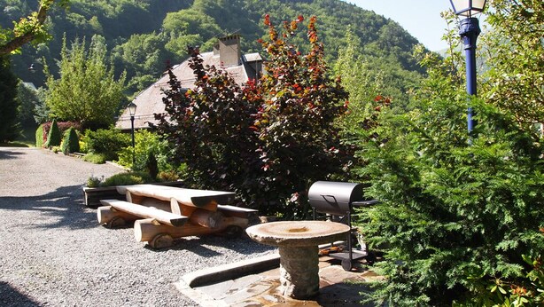 Un área de estar al aire libre de estilo rústico con una mesa de piedra y bancos, rodeada de exuberante vegetación y un paisaje de montañas.