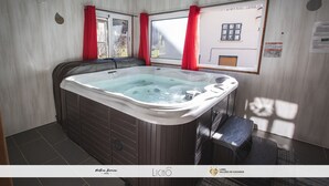 Un jacuzzi en una habitación con paredes de madera, una ventana con cortinas rojas y vistas a un edificio.